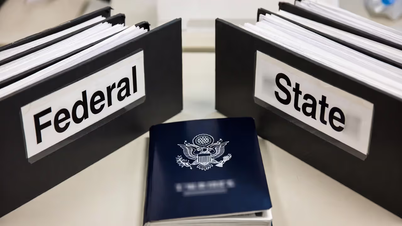 Two stacks of documents representing federal and state authority with a constitution book between them.